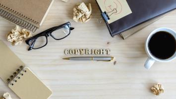 A birds eye view of a desk with reading glasses, notepads, a cup of coffee and scrunched up notes on it with the text "Copyright" in the centre.