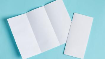 Folded, blank pieces of white paper on a light blue background resembling flyers or brochures.